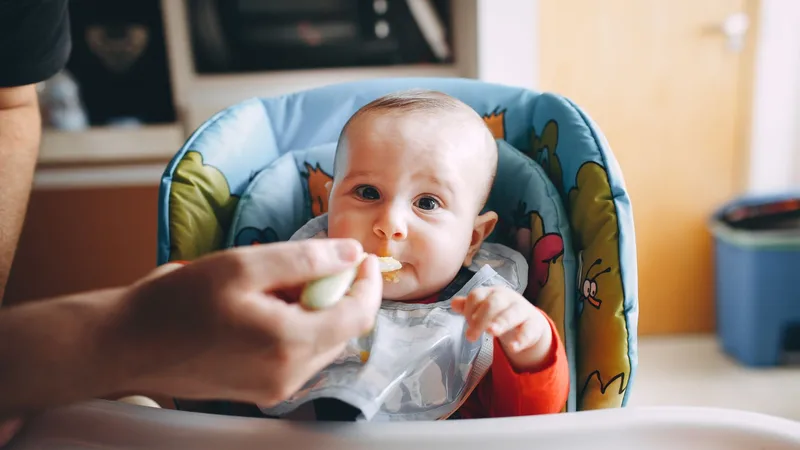 Ek gıdaya geçişte mama sandalyesindeki bebeğe küçük kaşıkla yumuşak yiyecek sunan anne